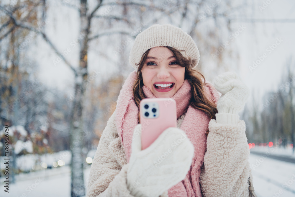 Fototapeta premium Excited young woman taking a selfie outdoors during a snowy winter day, enjoying the festive season