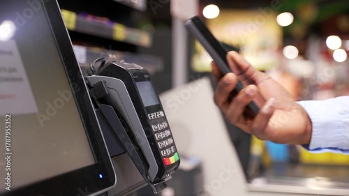 Close up african american male hand with a phone using a contactless NFC terminal to pay for purchases at counter in store. Male buyer pays for goods online. using a smartphone in the supermarket. pos