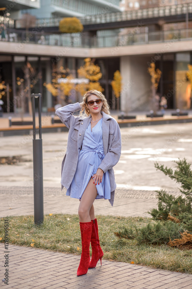 Naklejka premium Portrait of a young blonde woman in a red hat and boots on an autumn walk in the city