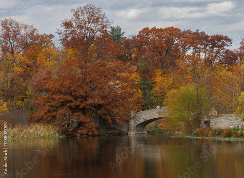 Beautiful fall colors with orange and yellow trees surrounding a serene pond with a stone bridge in Verona Park New Jersey during autumn season