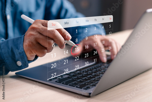 Fotografía Closeup of hands using stylus on a digital calendar over a laptop, highlighting a specific date