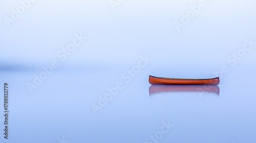 A solitary red canoe resting on a vast tranquil blue lake surface under soft light