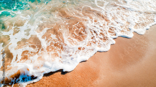 Fototapeta Naklejka Na Ścianę i Meble -  Ocean wave with white foam gently washing onto a pristine sandy beach, showing clear turquoise water and wet golden sand