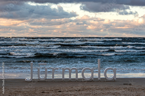 Fototapeta Naklejka Na Ścianę i Meble -  Waves crashing near the Jurmala sign on the beach during sunset in Latvia