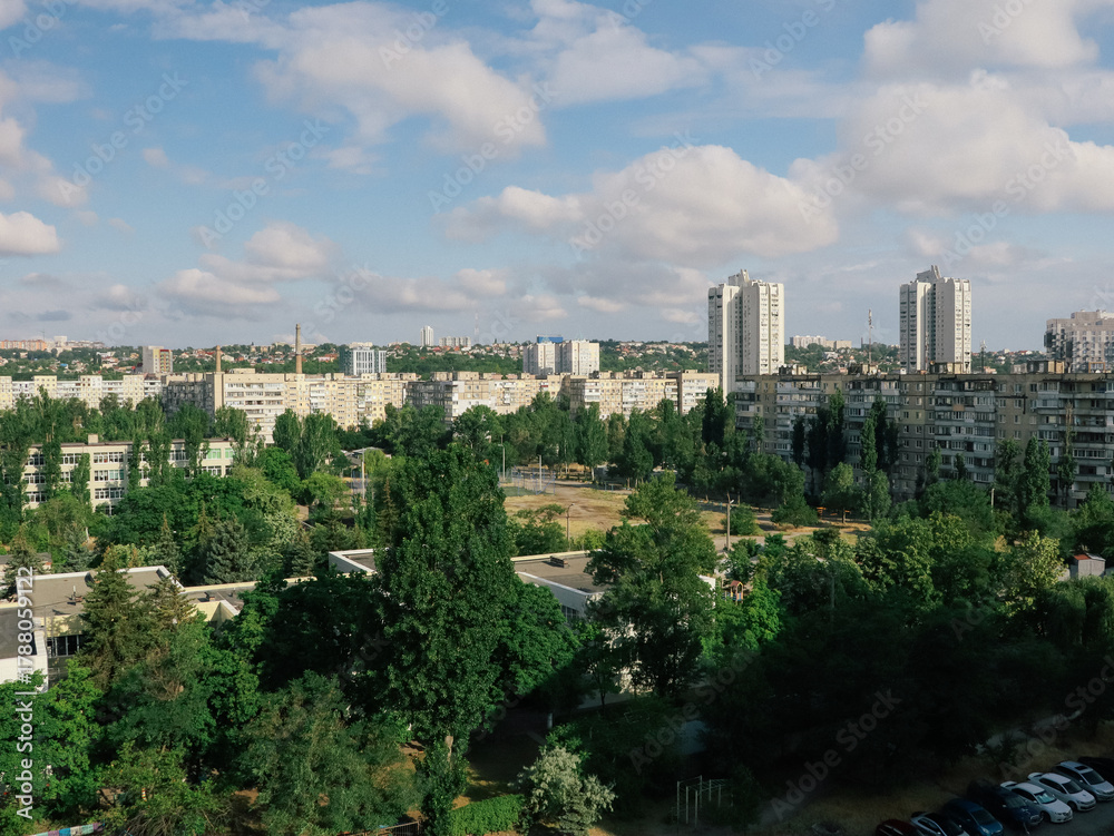 Obraz premium Cityscape view of residential buildings and green trees under a blue sky. This aerial view showcases a city with apartment buildings and lush green trees on a sunny day