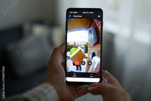 Closeup of a woman using a smartphone app to watch a delivery man dropping off a package