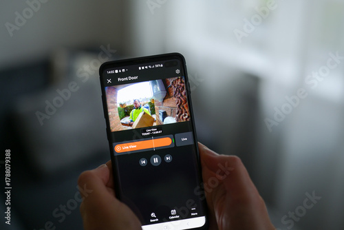 Closeup of a woman using a smartphone app to watch a delivery man dropping off a package