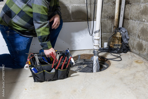 handyman with tool bag looking at home repair in basement at sum pump well