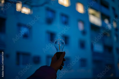 A lamp without light in a hand against the background of a multi-story building in the evening. Power outages due to the war in Ukraine.