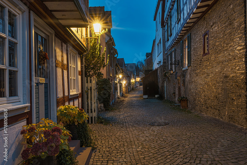 Fototapeta Naklejka Na Ścianę i Meble -  A small, romantic alley in the old town of Idstein in the Taunus region of Hesse, illuminated by streetlights in the evening.