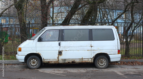 Old rusty white minivan parked near a metal lattice fence, Iskrovsky Prospekt, Saint Petersburg, Russia, November 11, 2025