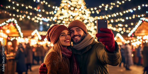 happy smiling couple taking selfie at a Christmas market at night with Christmas decorations in the background