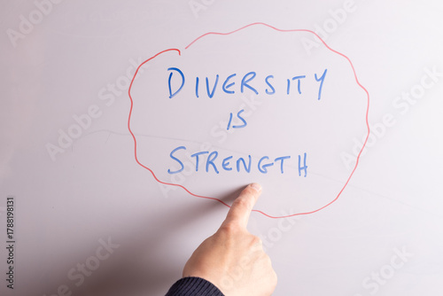 An HR business professional is pointing to the phrase Diversity is Strength on a whiteboard in blue marker pen, ideal for HR, DEI, recruitment, and business workplace presentations.