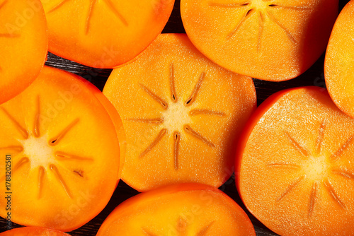 sliced persimmon on black wood background top view