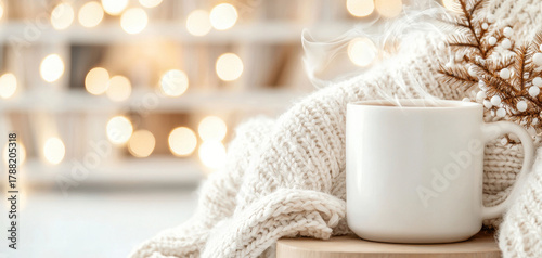 Cozy winter mug warm knit blanket steaming coffee cup soft bokeh lights neutral beige decor wooden stool accent holiday pine branch