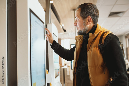 Man using self-service touchscreen kiosk in modern restaurant, interacting with digital ordering system, choosing items on interactive display, concept of technology, automation, and customer convenie