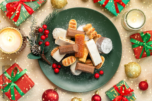 Top view of nougat Christmas sweet,mantecados and polvorones on a green plate with Christmas ornaments. Assortment of Christmas sweets typical in Spain