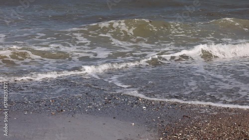 Gentle baltic sea waves with white foam washing up onto a dark pebble and gravel beach shoreline