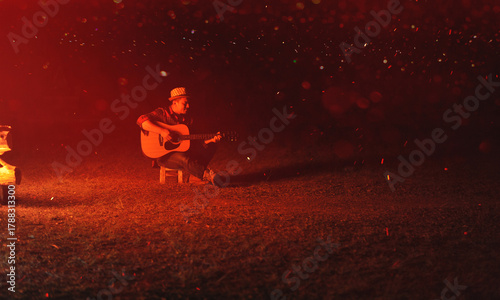Musicians play guitars by the campfire at night, relaxing by playing music and enjoying themselves.