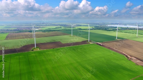 The drone glides smoothly over wide fields and several wind turbines. Clear visibility, green landscapes, and soft summer light define the scene.