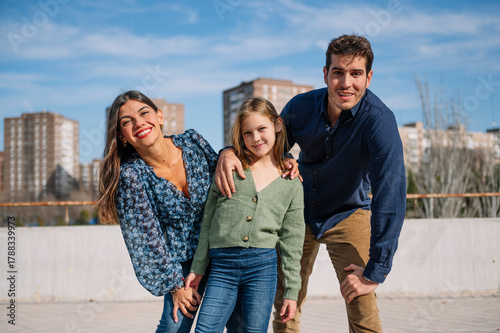 Cheerful parents with their daughter posing together under a clear sky