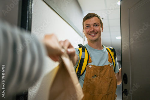 Male delivery person smiling, presenting a package to a customer at their home entrance, representing reliable e-commerce, express shipping, and convenient modern service industry