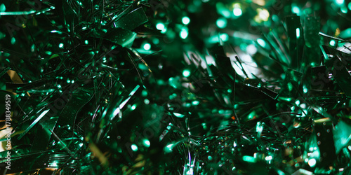 Macro abstract background of shiny dark green tinsel strands interspersed with bright green bokeh light spots.