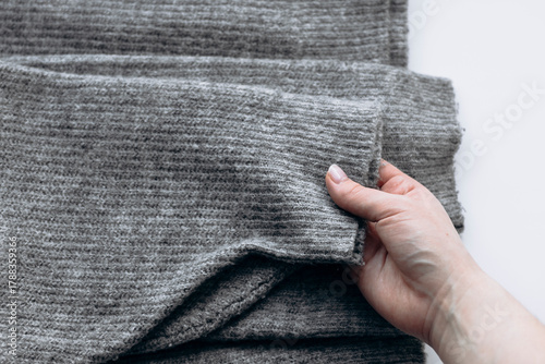 Woman holding gray sweater with pilling on white background.