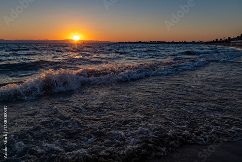 Fototapeta Naklejka Na Ścianę i Meble -  Low evening sun over the Mediterranean. Backlight highlights the waves, sparkling droplets and foam shimmer in warm orange tones. Gradient sky and glowing reflections create a calm summer mood. Turkey