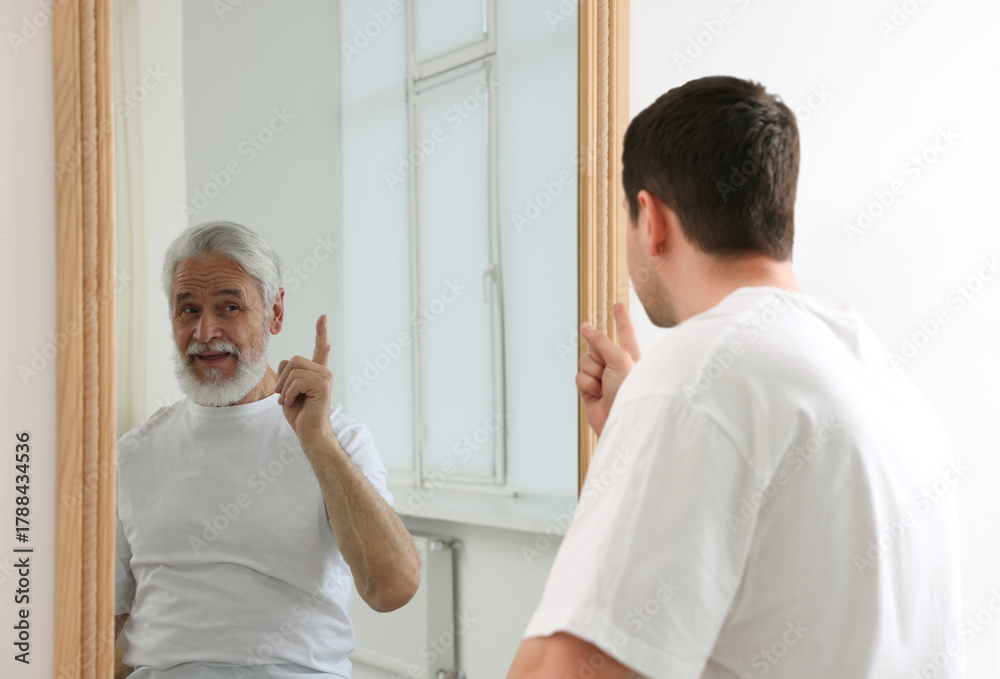 Obraz premium Young man seeing himself as senior in mirror. Concept of personality, past and future, flow of time, age
