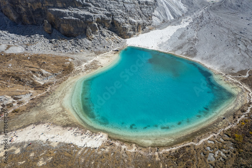 Turquoise alpine lake nestled among dramatic snow-capped mountains. A serene trekking destination in Yading Nature Reserve, Daocheng.