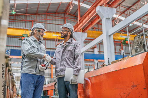 Two industrial workers inspecting machinery in a factory. Teamwork, precision, and safety gear highlight professional collaboration in metal production and mechanical maintenance.