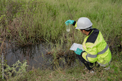 Tableau sur toile Environmental engineer wearing safety gear collecting water sample from polluted pond for contamination analysis, environmental testing, and ecological impact assessment in natural outdoor setting