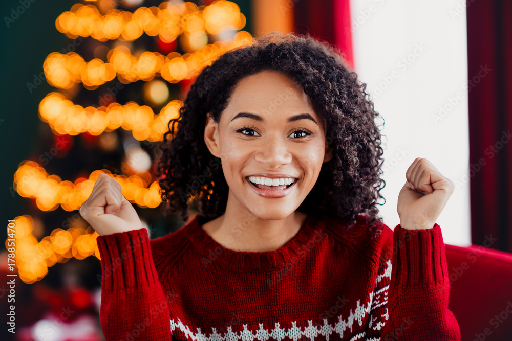 Fototapeta premium Funny festive moment as a woman in a red sweater cheers at home with a glowing Christmas tree and warm holiday vibes