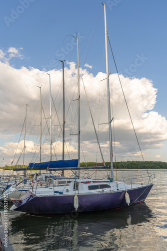 Peaceful marina with sailboats moored on tranquil lake under dramatic clouds and mirrored reflections in nature. Sailboats docked on calm water with reflections and cloudy sky.