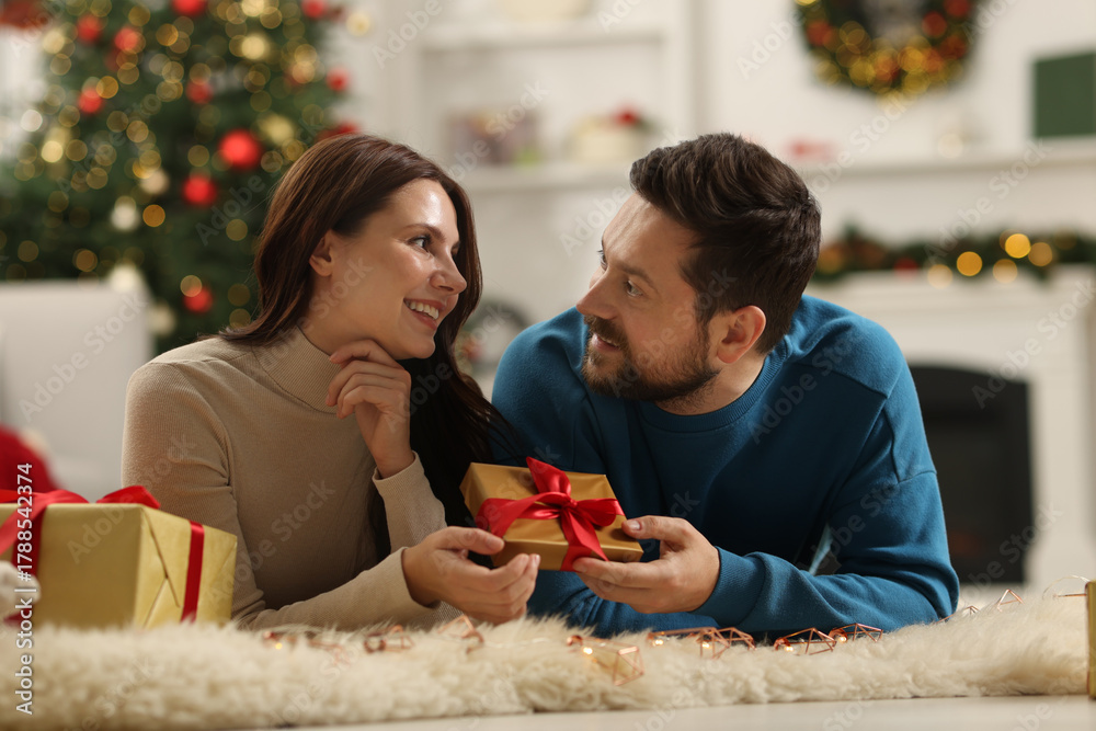 Obraz premium Happy couple with gift box spending time together in room decorated for Christmas