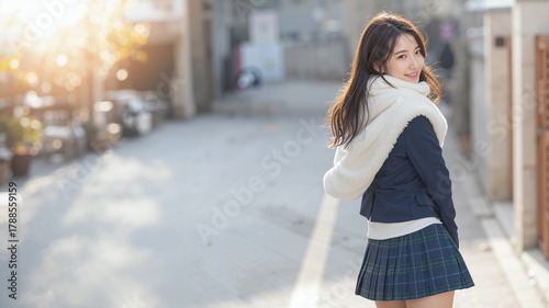Happy Korean student in winter uniform and white fur shawl smiles back while walking to school on quiet, peaceful morning street