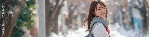 Japanese schoolgirl in winter uniform and gray fur shawl smiles back while walking on snowy street with trees, serene atmosphere
