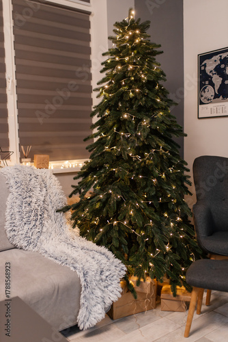 home christmas decor. living room interior for new years celebration. festive wreath, christmas tree. white sheets. couch, blanket, garland, presents. grey. minimalistic