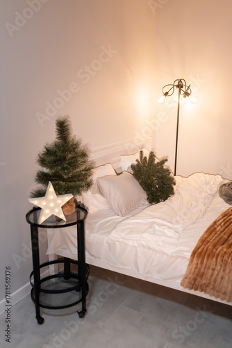 bedroom christmas decor. home interior for new years celebration. festive wreath, christmas tree. white sheets. pretty