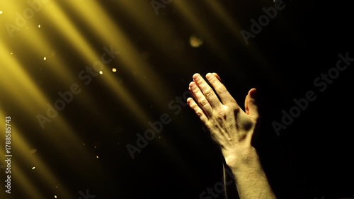 A man clasps his hands in prayer, enveloped in yellow divine light and fairy dust falling from above. 4K conceptual slow motion video 60 fps.