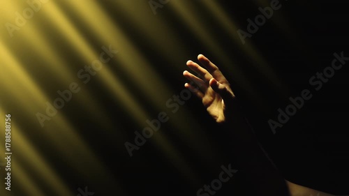 A man's hand reaches out to the shimmering divine rays of bright golden light in the darkness. 4K concept slow motion video 60 fps.