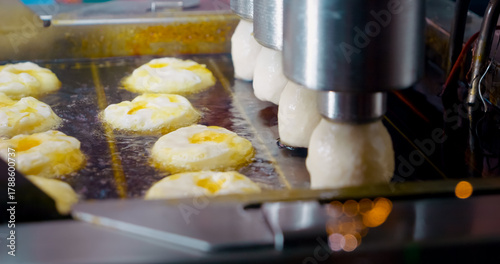 Modern industrial machinery executing systematic doughnut production, systematically deep frying pastries in large scale boiling oil processing line