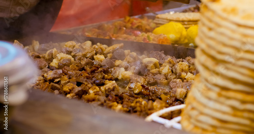 Fototapeta Naklejka Na Ścianę i Meble -  Street vendor grilling small meat pieces on sizzling hot plate, using spatula with professional skill while creating aromatic street food dish