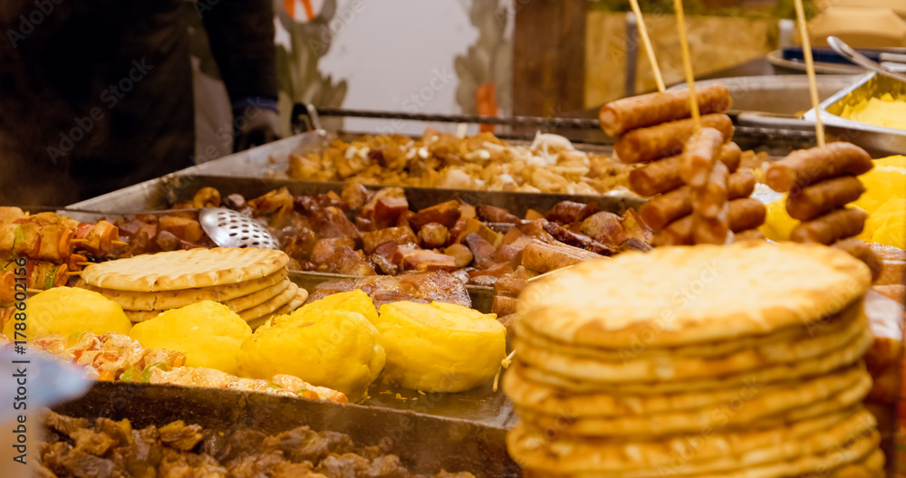 Fototapeta premium Romanian street food, including polenta, mici, sausages, and pita bread, cooking on a large hot plate