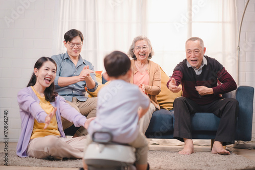 Happy Asian multigenerational family celebrating together at home with toddler riding toy car, showing joy, bonding, and family love in a warm living room environment.