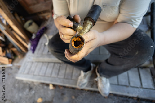 A cross-section of an old clogged water pipe A man holds a section of an old metal water pipe, examining a thick layer of rust and mineral deposits indicating severe corrosion in the plumbing system.