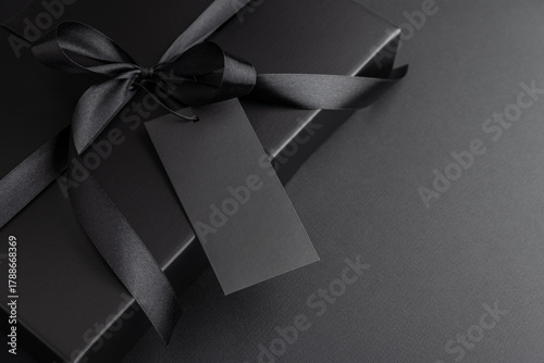 Black Gift Box with Satin Ribbon and Blank Tag on Dark Background