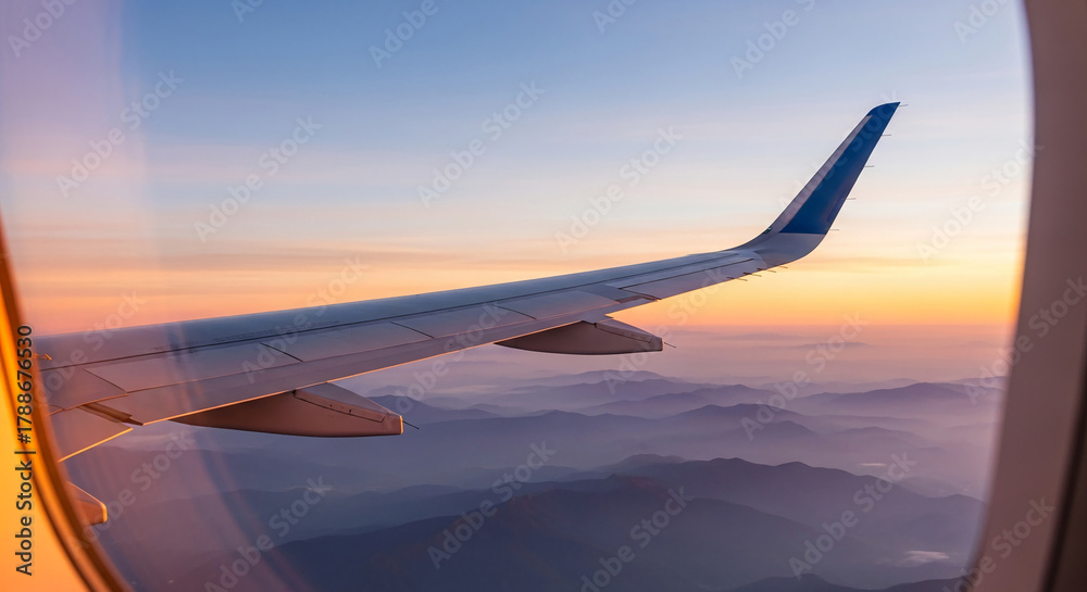 Fototapeta premium View from airplane window showing wing and distant mountains at sunset, representing travel, freedom, and adventure, perfect for vacation concepts