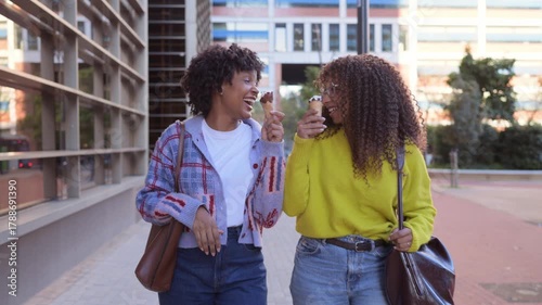 Happy young women friends eating ice cream walking on a city street